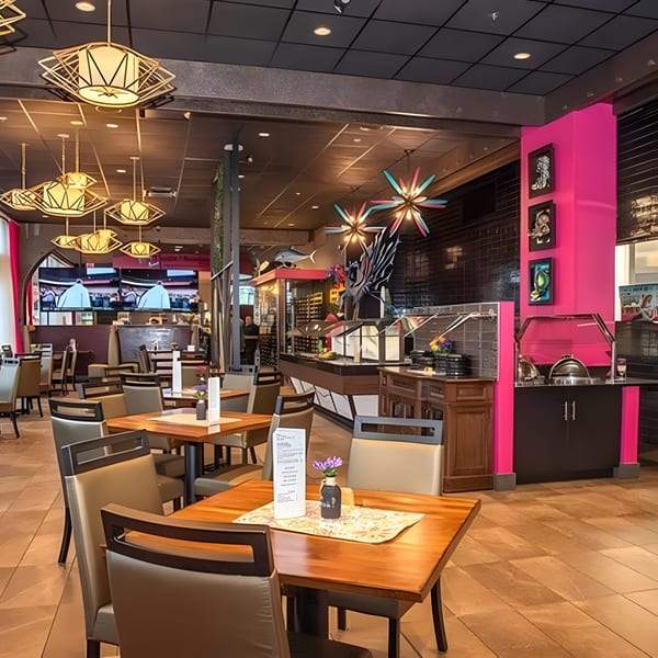 A vibrant restaurant interior with modern lighting, wooden tables, and a buffet area with hot pink accents.