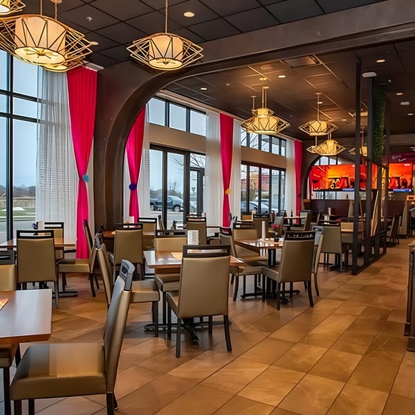 Modern restaurant interior with empty tables, beige chairs, large windows, and decorative pink curtains.