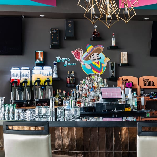 A vibrant bar with a "Krazy Juan" logo, margarita machines, liquor bottles, and bar stools.