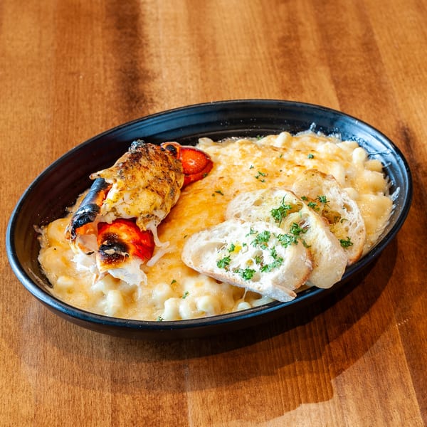 Lobster mac and cheese with toasted bread slices and parsley in a black bowl on a wooden table.