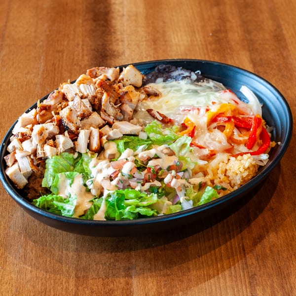A colorful chicken bowl with lettuce, pico de gallo, rice, beans, cheese, and peppers.