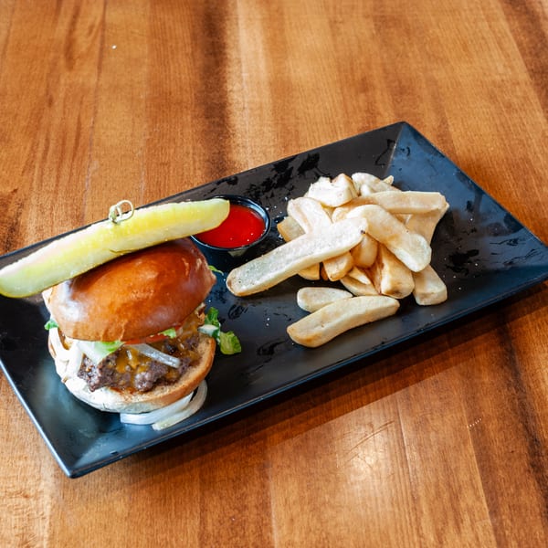 A cheeseburger with lettuce, tomato, onion, and a pickle spear, served with fries and ketchup on a black plate.